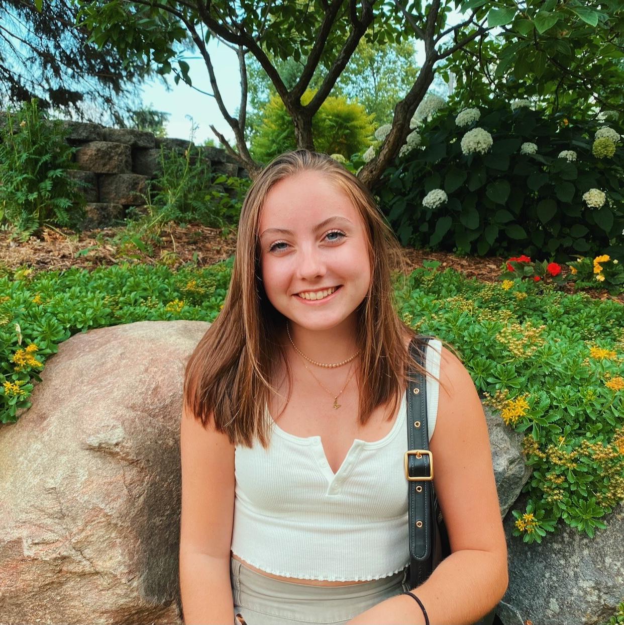 brooke outside in a blue tanktop and purse with an array of colorful flowers in the background